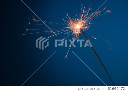 Burning festive Christmas sparkler on blue background with a lot of sparks Burning festive Christmas sparkler on blue background with a lot of sparks 61669472