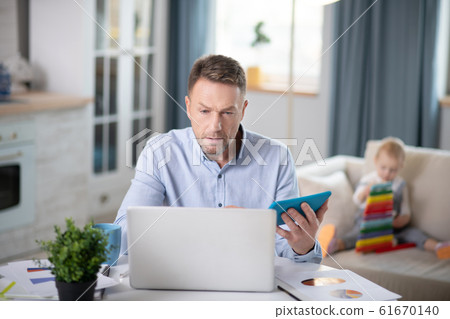 Bearded man in a blue shirt looking involved working on his laptop Bearded man in a blue shirt looking involved working on his laptop 61670140