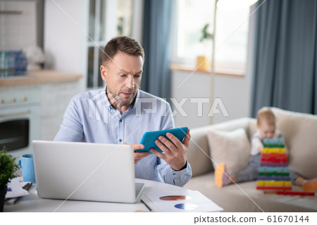 Bearded man in a blue shirt looking concentrated looking at the tablet Bearded man in a blue shirt looking concentrated looking at the tablet 61670144