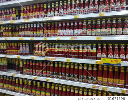 Chili and tomato sauce in packed for sale in clear glass bottle.  Displayed on metal rack in supermarket.  61671396