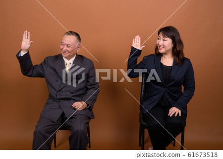 Happy mature Asian businessman and mature Asian businesswoman waving hands together 61673518