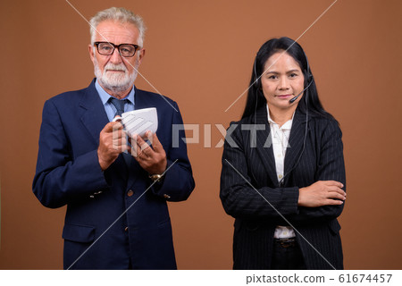 Mature multi-ethnic business couple against brown background Mature multi-ethnic business couple against brown background 61674457