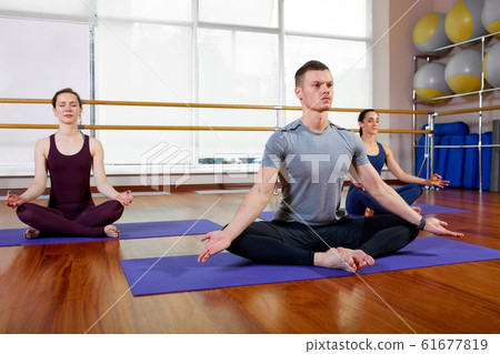 Group of sporty people sitting on mats and doing exercise for relaxation Group of sporty people sitting on mats and doing exercise for relaxation 61677819