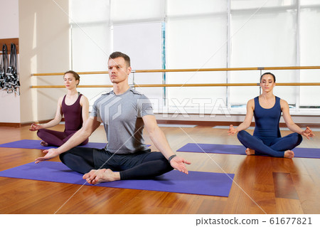 Group of sporty people sitting on mats and doing exercise for relaxation Group of sporty people sitting on mats and doing exercise for relaxation 61677821