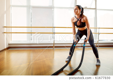 Fit, sporty and athletic sportswoman working in a gym. Woman training using battle ropes. Sports, athletics and fitness concept. 61677830