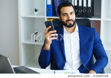 Business. Happy Business Man Sits at the Light Office and Holds 61680599