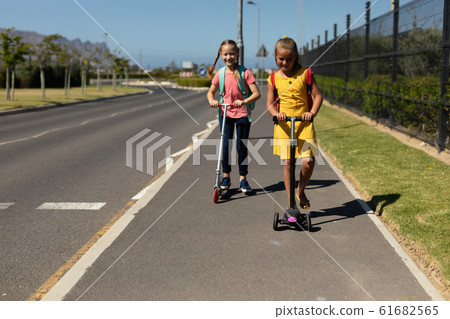 Caucasian schoolgirls riding push scooters Caucasian schoolgirls riding push scooters 61682565