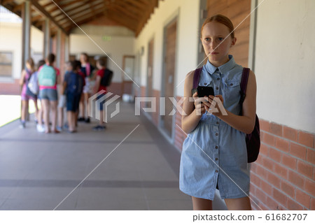 schoolgirl standing in the schoolyard at elementary school using a smartphone 61682707