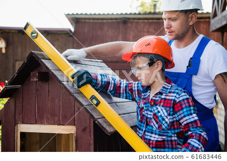 The boy holds the building level, checking the accuracy of the dog house roof. 61683446