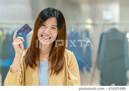 Portrait Asian woman holding and presenting the credit card for online shopping in department store over the clothes shop store background, technology money wallet and online payment concept Portrait Asian woman holding and presenting the credit card for online shopping in department store over the clothes shop store background, technology money wallet and online payment concept 61685986
