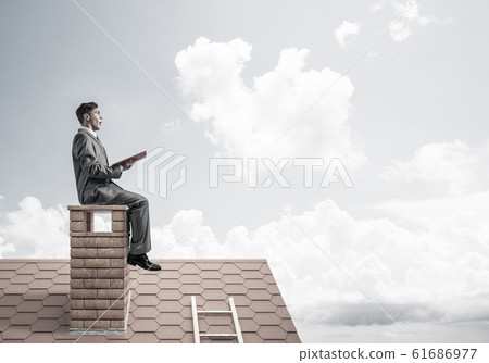 Student guy in suit on brick house roof reading book 61686977