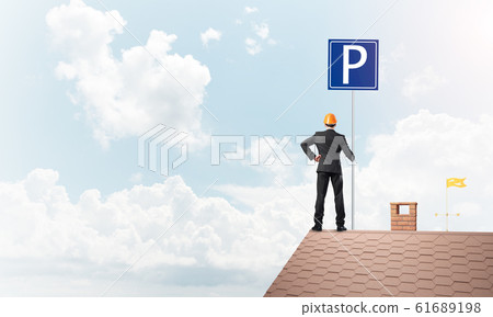 Young businessman with parking sign standing on brick roof. Mixed media 61689198