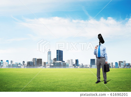 Camera headed man standing on green grass against modern cityscape Camera headed man standing on green grass against modern cityscape 61690201
