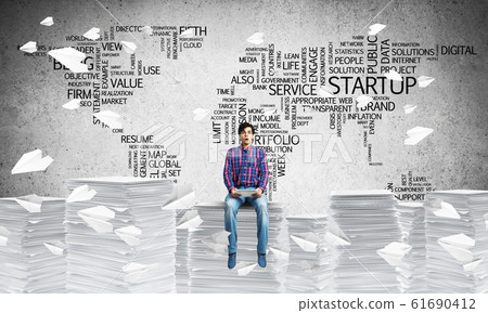 Attractive man sitting on pile of paper documents. Attractive man sitting on pile of paper documents. 61690412