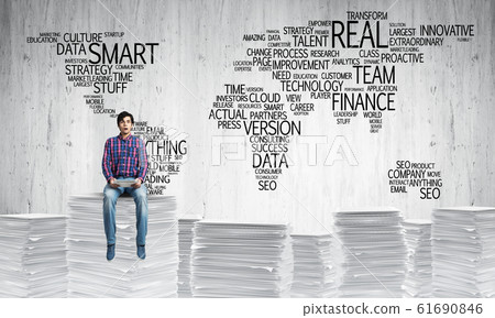 Attractive man sitting on pile of paper documents. Attractive man sitting on pile of paper documents. 61690846