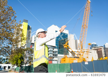 Senior foreman in glasses doing his job at building area on sunny day Senior foreman in glasses doing his job at building area on sunny day 61691470