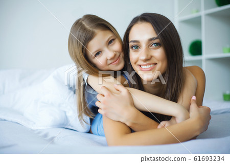 Woman and young girl lying in bed smiling Woman and young girl lying in bed smiling 61693234
