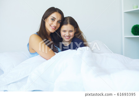 Woman and young girl lying in bed smiling Woman and young girl lying in bed smiling 61693395