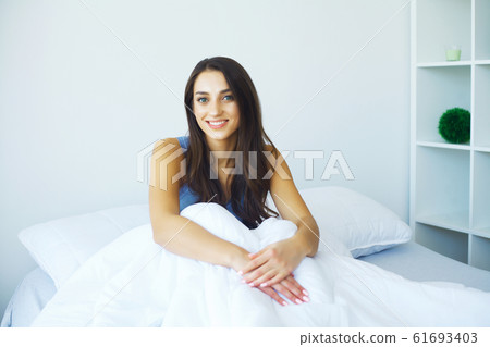 Beautiful woman has woken up and is sitting on a white bed Beautiful woman has woken up and is sitting on a white bed 61693403