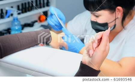 Manicurist files a nail with a nail file to a client. Manicure process, nail extension. close-up Manicurist files a nail with a nail file to a client. Manicure process, nail extension. close-up 61693546