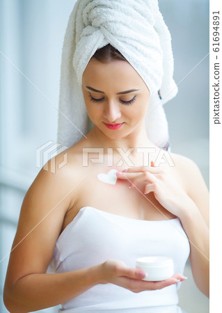 Studio shot of beautiful young woman applying moisturizer cream onto her face in modern bathroom 61694891