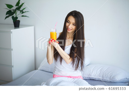 Cheerful woman drinking an orange juice sitting on her bed 61695333