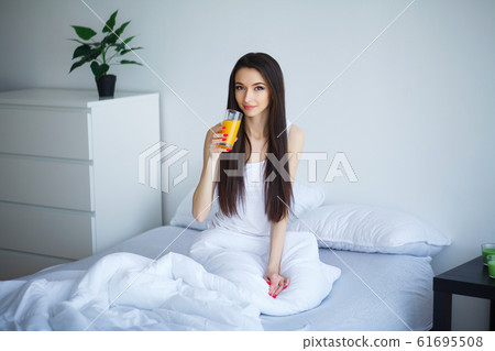Cheerful woman drinking an orange juice sitting on her bed at home 61695508