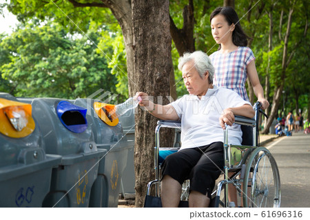 Asian little child girl or granddaughter and senior grandmother hand putting plastic water bottle in recycling bin,elderly tourist in wheelchair,hand throwing garbage in a trash bin,environmental prot Asian little child girl or granddaughter and senior grandmother hand putting plastic water bottle in recycling bin,elderly tourist in wheelchair,hand throwing garbage in a trash bin,environmental prot 61696316