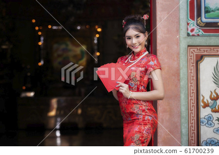 Chinese woman in a red cheongsam (qipao) dress holding red envelopes (hong bao) at shrine. 61700239