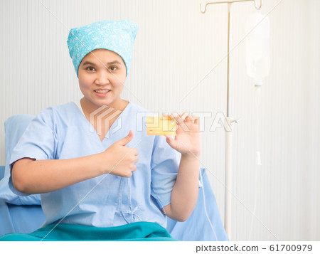 Portrait of a female patient sitting on the bed and holding credit card at clinic or hospital. Health insurance and service payment. Portrait of a female patient sitting on the bed and holding credit card at clinic or hospital. Health insurance and service payment. 61700979