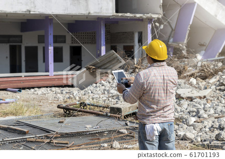 Engineer holding tablet is checking for destruction, demolishing building. 61701193