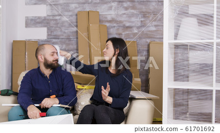 Girlfriend hitting boyfriend with instructions while assembling furniture Girlfriend hitting boyfriend with instructions while assembling furniture 61701692