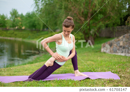 A young sports girl practices yoga on a green lawn A young sports girl practices yoga on a green lawn 61708147