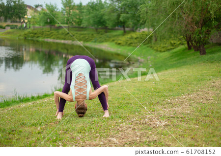 A young sports girl practices yoga on a green lawn A young sports girl practices yoga on a green lawn 61708152