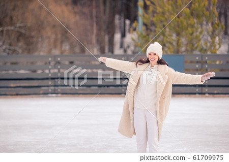 Smiling young girl skating on ice rink outdoors 61709975