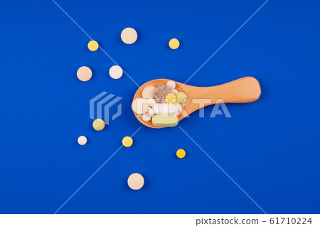 Medical pills with a wooden spoon on a blue background 61710224