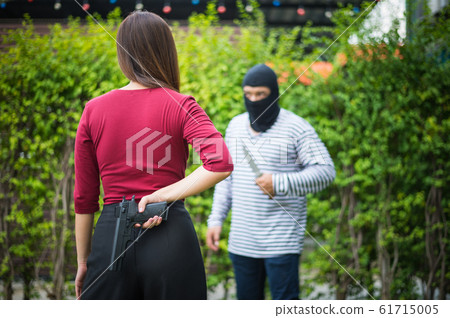 Criminal or Bandit wear black mask use knife trying to rob money from woman but she hide gun behind her, concept of winner, fighting, usurpation. 61715005