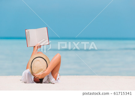 Portrait of a young woman relaxing on the beach, reading a book 61715341