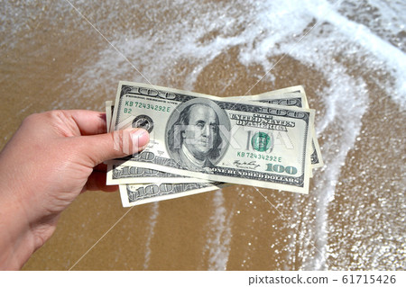 Girl holding a money bill of 300 dollars on background of sea waves Girl holding a money bill of 300 dollars on background of sea waves 61715426