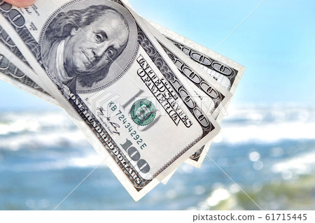 Girl holding money bill of 300 dollars on background of sea ocean Girl holding money bill of 300 dollars on background of sea ocean 61715445