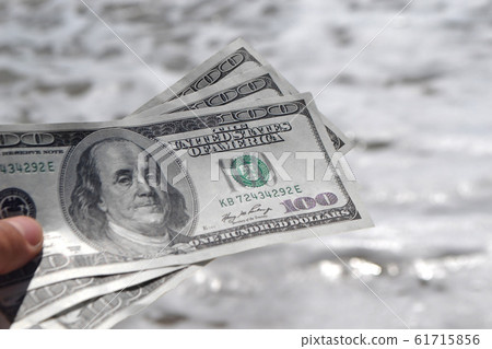 Girl holding money bill of 300 dollars on background of sea ocean Girl holding money bill of 300 dollars on background of sea ocean 61715856