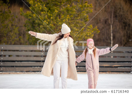 Little adorable girl with her mother skating on ice-rink 61716340