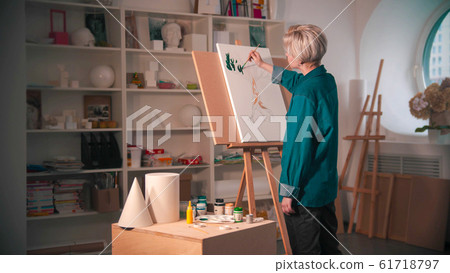 A young woman artist with short hair painting upper branches of tree in green color in the art studio A young woman artist with short hair painting upper branches of tree in green color in the art studio 61718797
