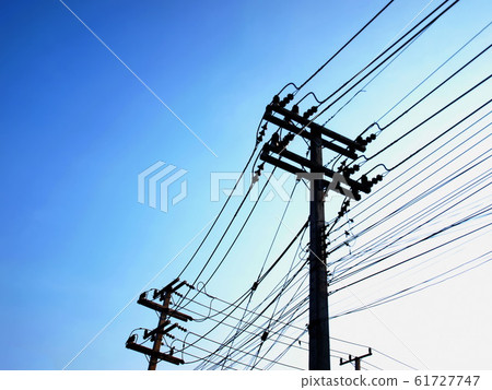 Silhouettes of high tension and low tension power lines on poles. On the bright blue morning sky background with copy space. Selective focus Silhouettes of high tension and low tension power lines on poles. On the bright blue morning sky background with copy space. Selective focus 61727747
