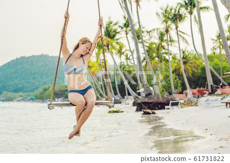 Vacation concept. Happy young woman sitting on swing enjoying sea view 61731822