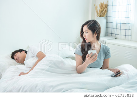wife spying the phone of her husband while man sleeping in bed at home. 61733038