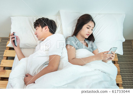 Young asian couple in bed using phone lying back to each other.relationship problem with technology. Young asian couple in bed using phone lying back to each other.relationship problem with technology. 61733044