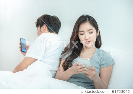 Asian couple in bed using phone lying backs to each other relationship problem with technology. Asian couple in bed using phone lying backs to each other relationship problem with technology. 61733045