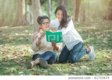 Elder asian mother and daughter read book in wood on green grass lawn,concept of happy family life 61733674
