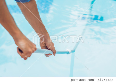 Cleaner of the swimming pool . Man in a blue shirt with cleaning equipment for swimming pools, sunny 61734588
